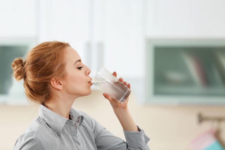 Woman drinking water to de-stress for your skin