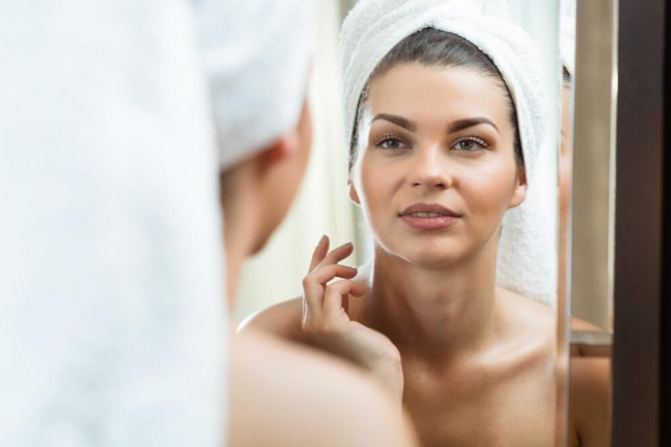 Woman looking at skin in mirror after reading our new year's resolutions for your skin